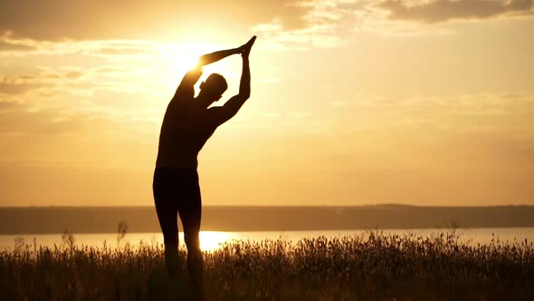 Silhouette of Young Sportive Man Practicing Yoga at Sunset