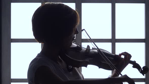 Girl Fingering the Strings Playing on a Violin Against the Window