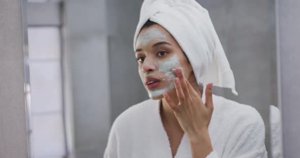 Mixed race woman applying face mask in bathroom