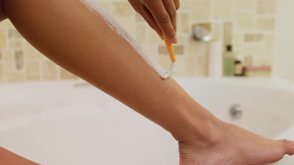 Young woman sitting on bathtub waxing her leg with razor in bathroom 4K 4k