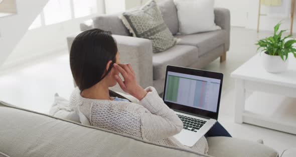 Back view of asian woman sitting on sofa and working remotely from home with laptop