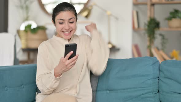 Indian Woman Celebrating Success on Smartphone on Sofa 