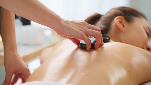 Asian young relaxing woman getting back massage therapy with hot stone.
