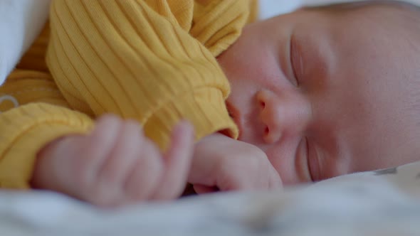 Tiny Newborn Baby in a Yellow Suit Sleeping Peacefully on His Side