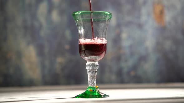 Rustic glass and painted wood table with red wine pouring into a glass with blue background.