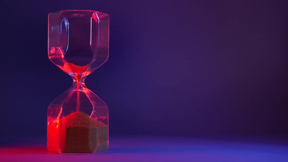 Glass Hourglass with Golden Sand on Purple Background