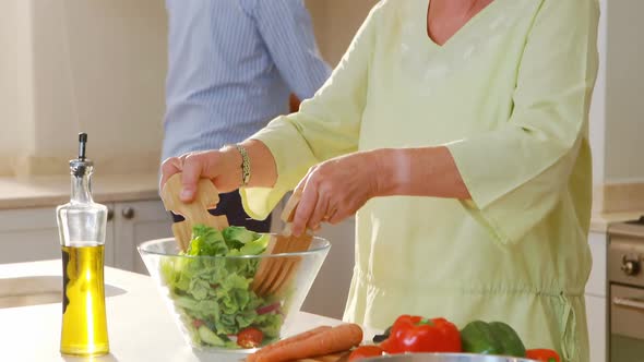 Senior couple talking while mixing a salad in kitchen