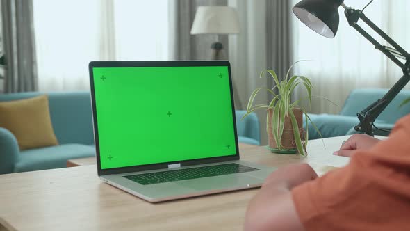 Young Asian Boy Sitting In A Wheelchair While Learning Online On Laptop With Green Screen