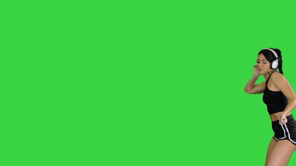 Young Happy Sportive Woman Dancing and Listening To Music in Headphones on a Green Screen, Chroma