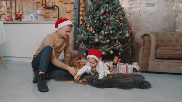 One Year Old Baby Sitting Near a Christmas Tree and Playing with Her Dad.