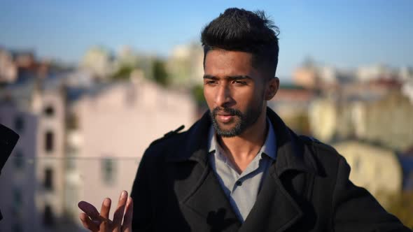 Young Confident Middle Eastern Man Talking with Friends Standing on Rooftop at Sunset