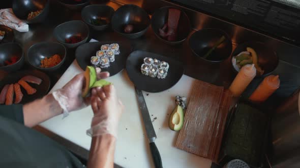 Professional Cook Cutting Avocado Into Thin Slices to Use As Decoration for a Sushi Dish