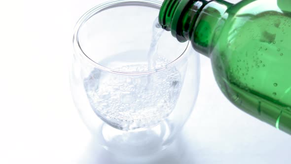 woman is pouring mineral water from green color plastic bottle in double wall insulated glass