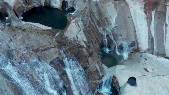 Top down aerial shot of cascading waterfalls and pools on a granite rock face