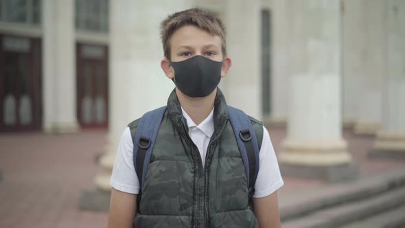 Schoolboy in Covid-19 Face Mask Looking at Camera and Walking To School Building. Portrait of