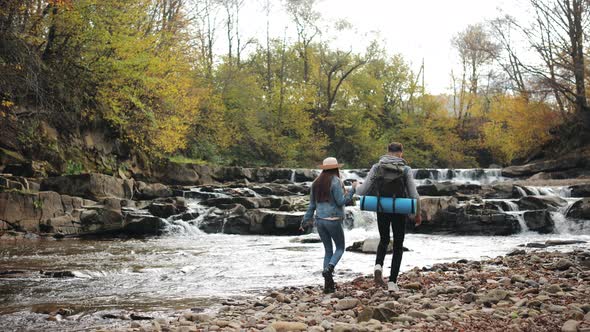 A Young Woman and a Man are Walking Along the Rocky Shore of a Mountain River