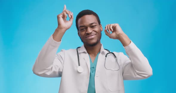 Happy African American Doctor in White Medical Coat Dancing Over Blue Studio Background