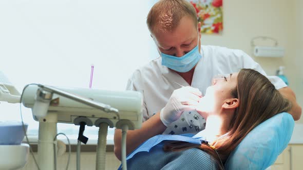 Dentist at work in the office. Male doctor treats teeth to a girl sitting in a chair