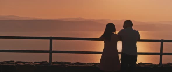 Young couple watching sunset above the lake from the viewing point. Medium shot.