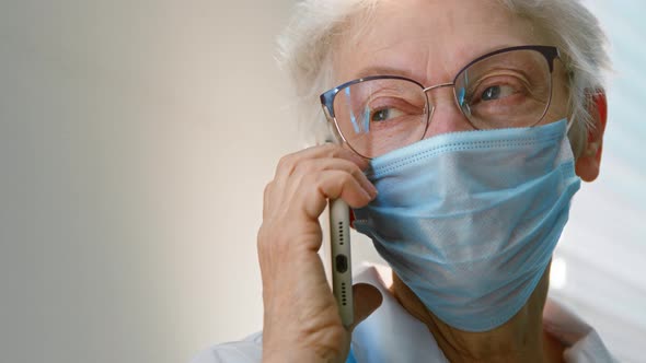 Mature woman doctor in protective mask and glasses talks on cell phone