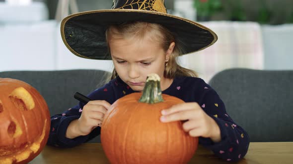 Girl in halloween costume drawing on pumpkin