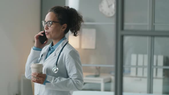 Female Doctor Holding Coffee and Talking on Phone at Work