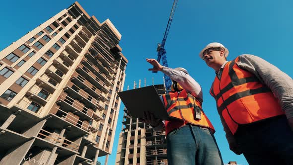 Construction Contractor Working on a Construction Site. Men Stand on a Site, Working with a Laptop. alt
