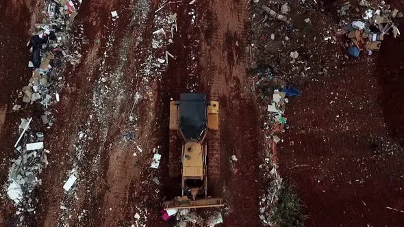 A bulldozer pushes trash at a landfill site - aerial straight down view