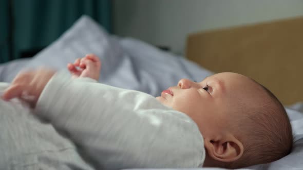 Baby Boy Lies on Bed and Moves Blowing Bubbles From Saliva