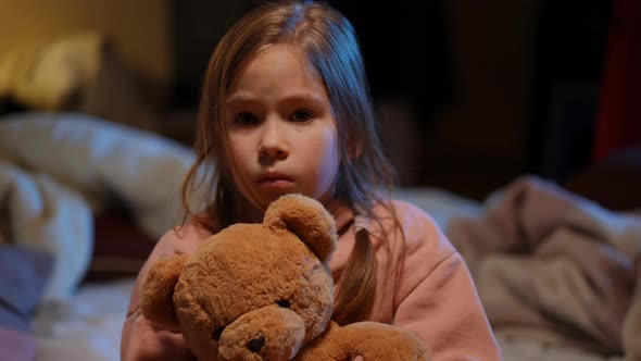 Closeup Frightened Cute Girl in Bomb Shelter Hugging Teddy Bear and Looking at Camera