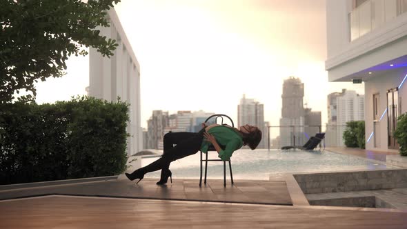 Dancer In High Heels And Green Jacket Posing On Chair At Poolside