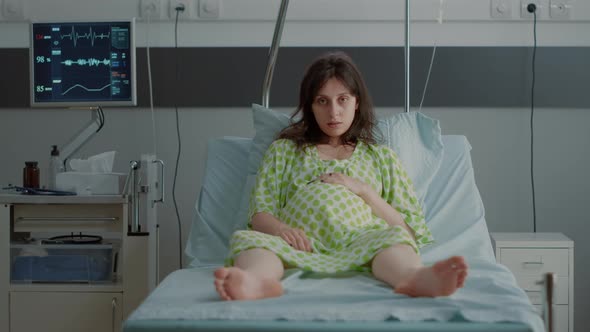 Portrait of Pregnant Person Sitting in Hospital Ward Bed