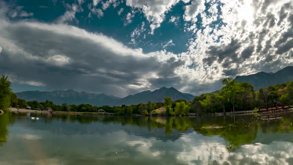 Cloudscape reflecting off the water in a pond with rocky mountains in the background - zoom in time