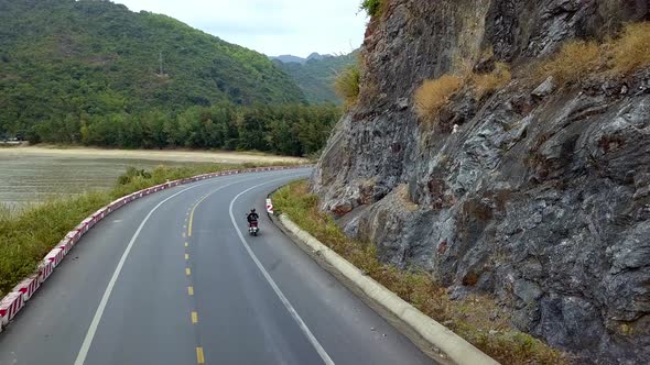 Woman on a moped riding on an island road near the coastline, Aerial follow behind shot