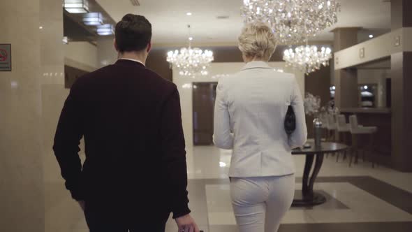 Back View of Male and Female Traveller Walking in Luxurious Vestibule