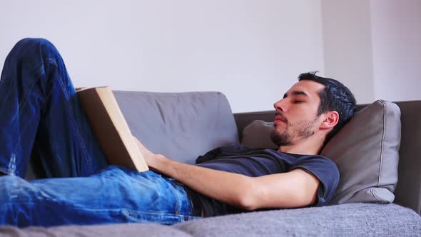 Young man lying down on sofa and using laptop computer. Candid view