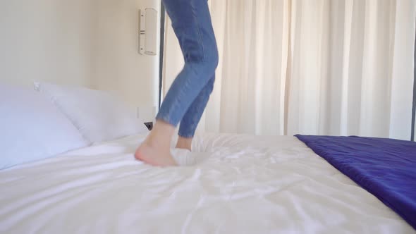 an unrecognizable woman without face with bare feet jumps on bed in bedroom