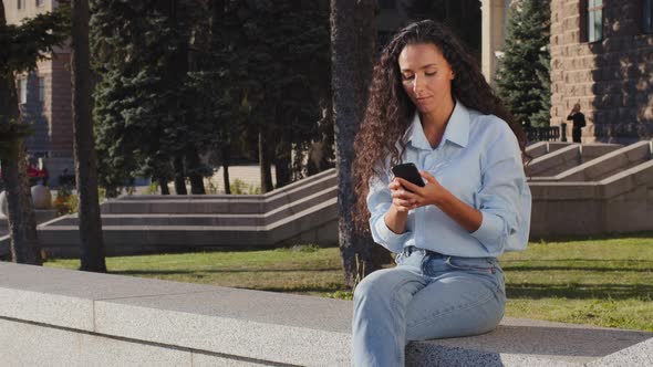 Young Beautiful Brunette Girl Woman Smiling Waiting Sitting in City Street Looking at Mobile Phone