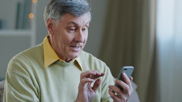 Mature Elderly Mature 60s Caucasian Man with Phone Male Grandfather Uses Mobile App at Home Buys