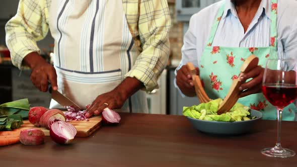 Senior man chopping vegetables while woman preparing salad in kitchen