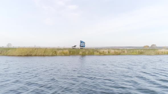 Camera flying along the rippled river with a driving truck