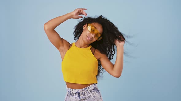 Afroamerican Model in Yellow Sunglasses is Smiling Dancing and Shaking Her Long Curly Hair While