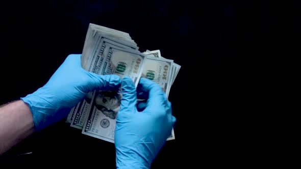 Nitrile gloved hands counting a stack of benjamins onto a black surface in slow motion.  Ideal for s