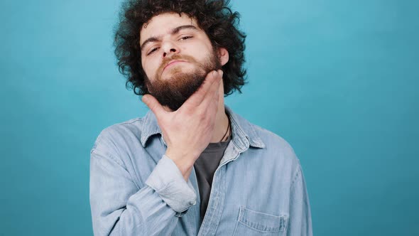 Hesitating Young Man Touches Beard with Hand Looking Ahead