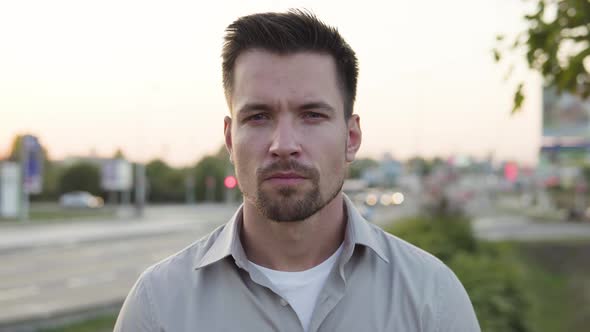 A Young Caucasian Man Looks Seriously at the Camera in an Urban Area  Closeup