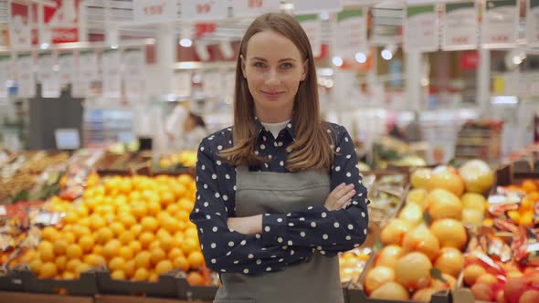 Portrait of a Female Worker in an Apron Against a Background of Fruits a Young Woman Crosses Her