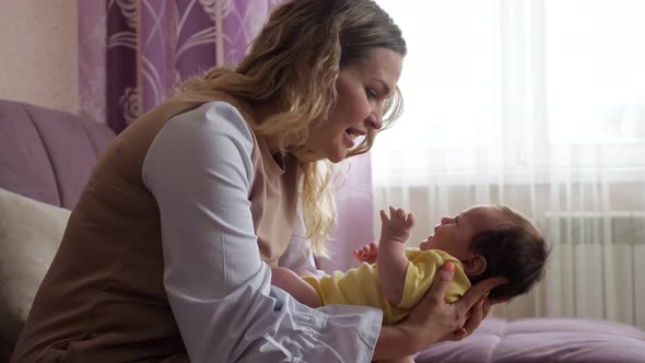 Young Blonde Mother Calms Down Crying Baby Girl on Sofa