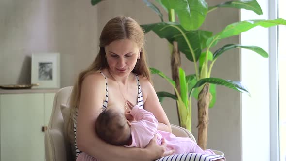 Young Mother Feeding Little Daughter and Sitting on Couch in Apartment Room Spbd