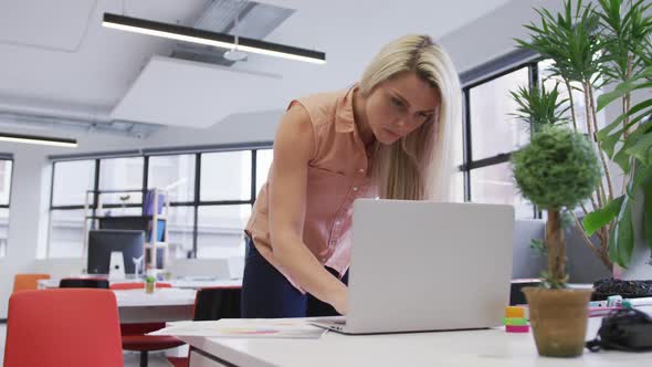 Caucasian businesswoman using a laptop going through paperwork in modern office