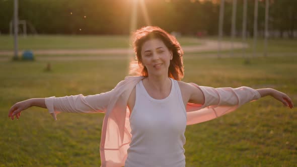 Positive Woman Raises Hands Enjoying Strong Wind on Meadow